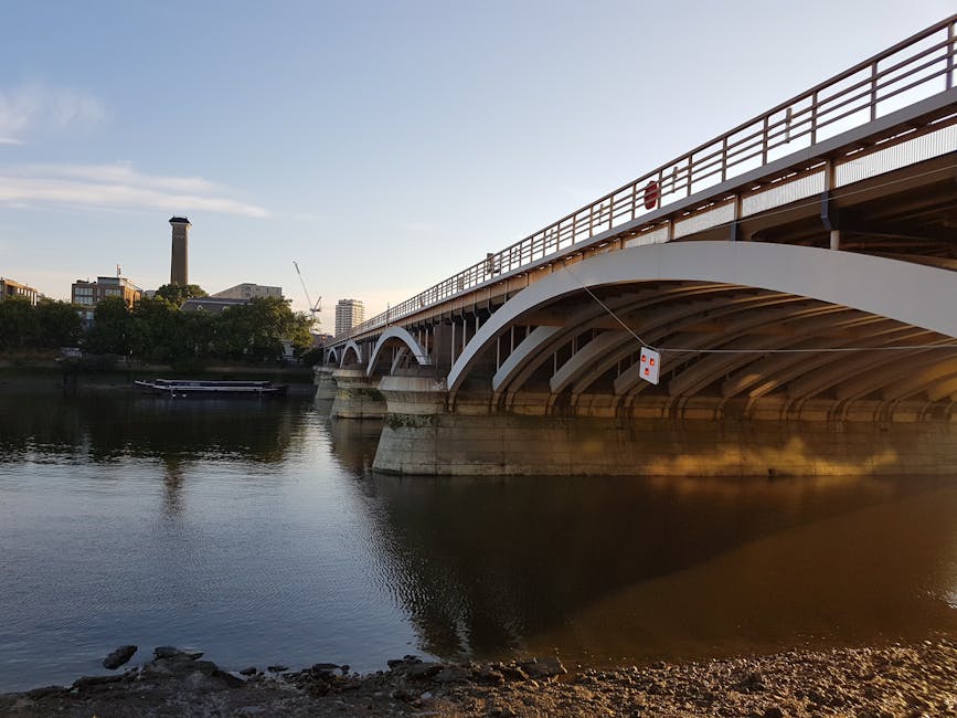 A detailed view of the Hammersmith Bridge's painted metal suspension structure, showing its tall, ornate towers and numerous white cables supporting the suspension. The bridge's surface includes weath